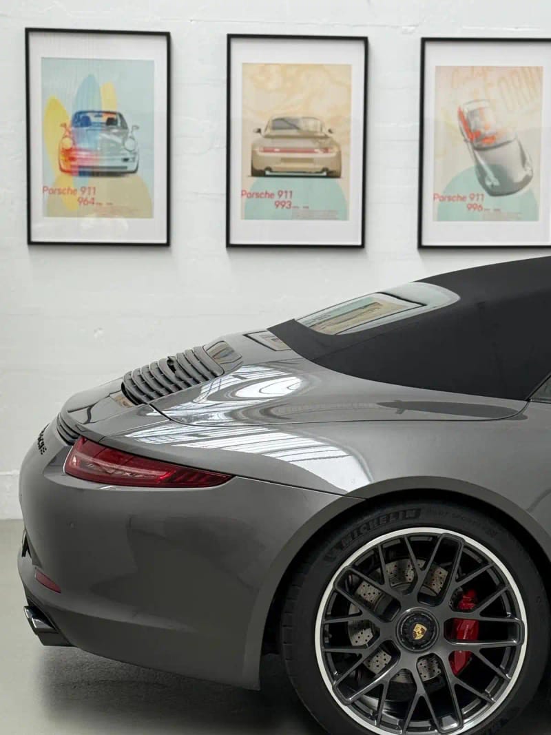 Heck eines grauen Porsche 911 vor gerahmten Porsche-Bildern im Showroom